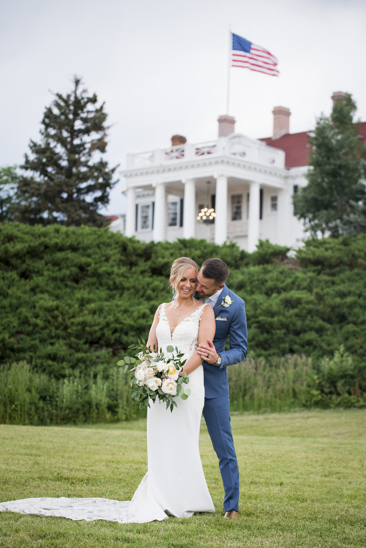 A groom kisses his bride from behind with The Manor House in the background.