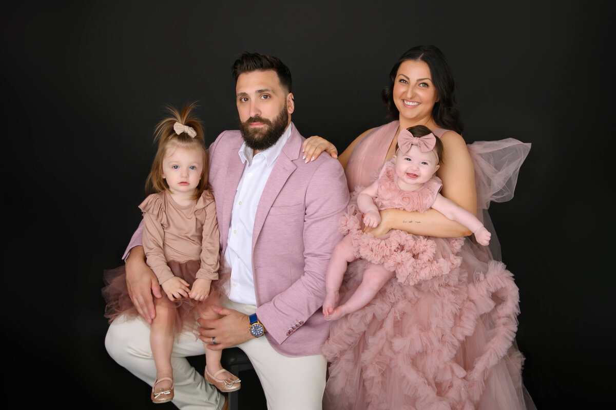 Up-close mom and dad holding their two young daughters all wearing pink for their studio family photos in Burlington, ON