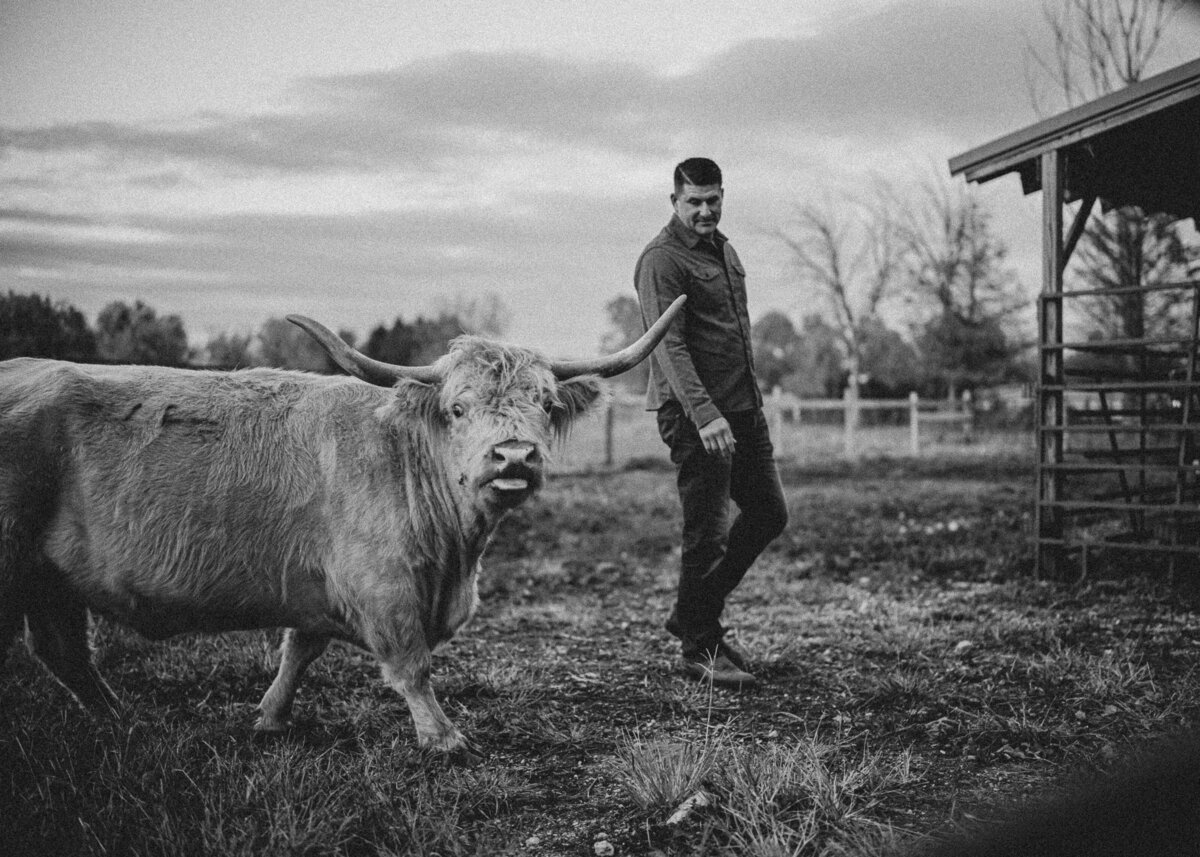 A black and white image of a farmer walking alongside his cow on his family farm.
