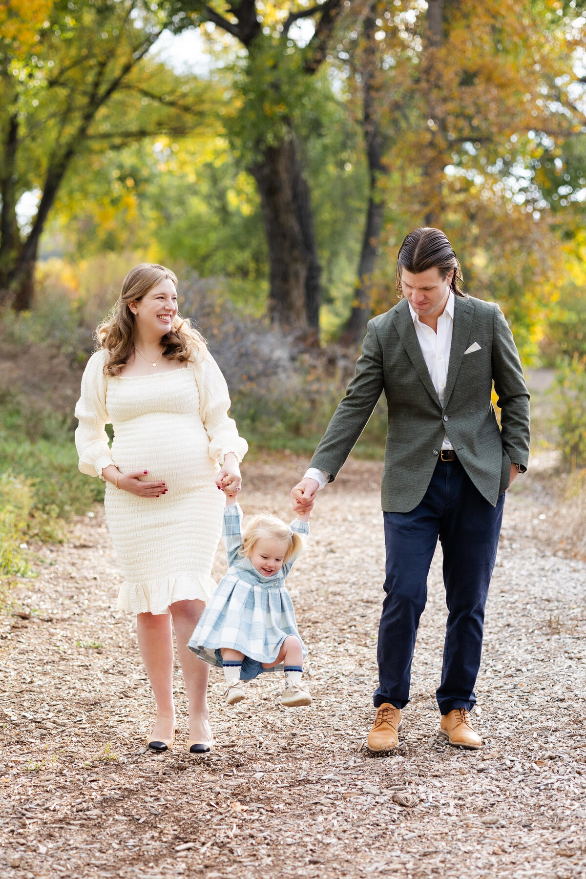 Mom and dad swing their toddler daughter between them as mom smiles at dad and dad smiles at their daughter.