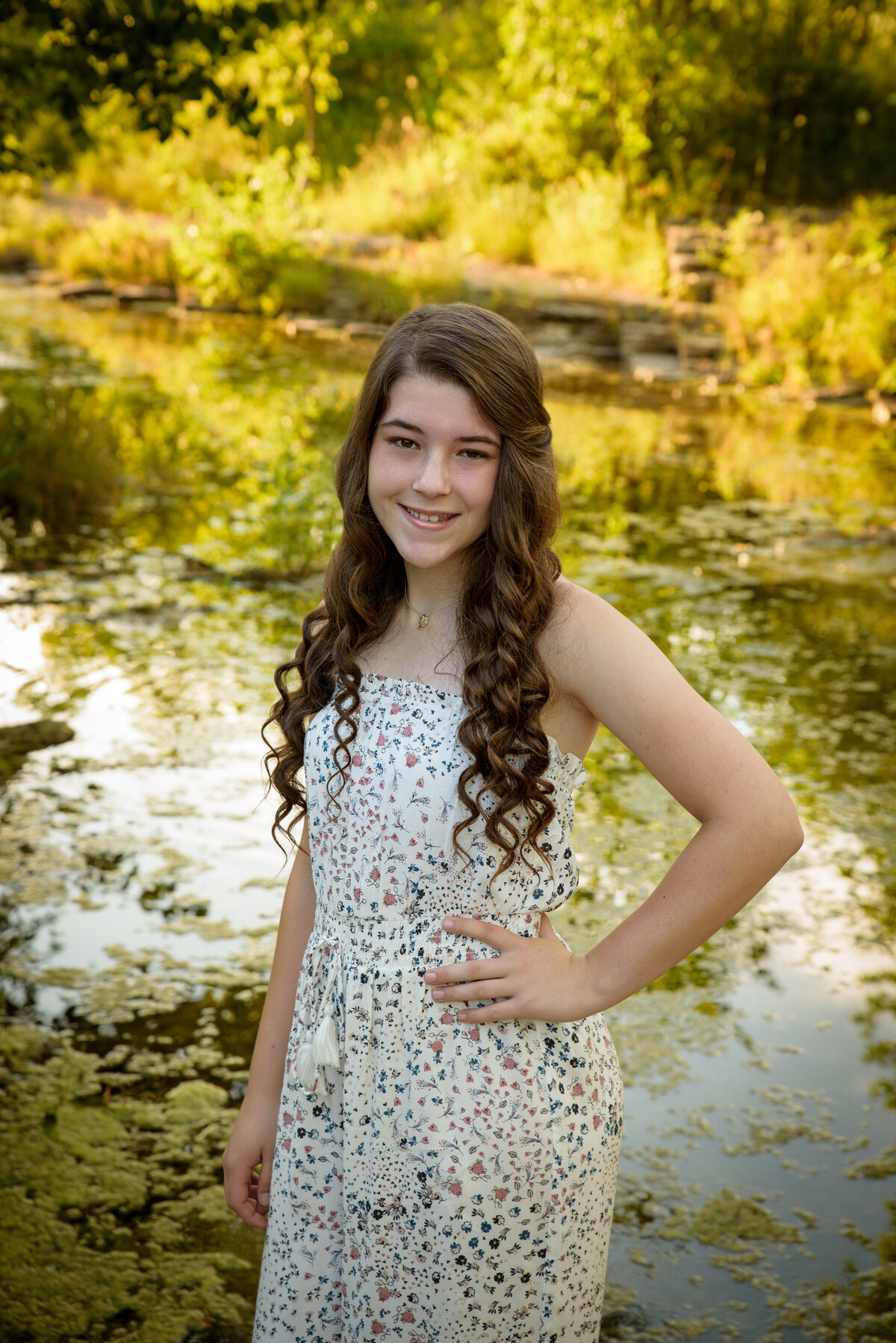 Teenage girl with long brown hair wearing a cream romper standing near the creek at Fonferek Glen County Park near Green Bay, Wisconsin