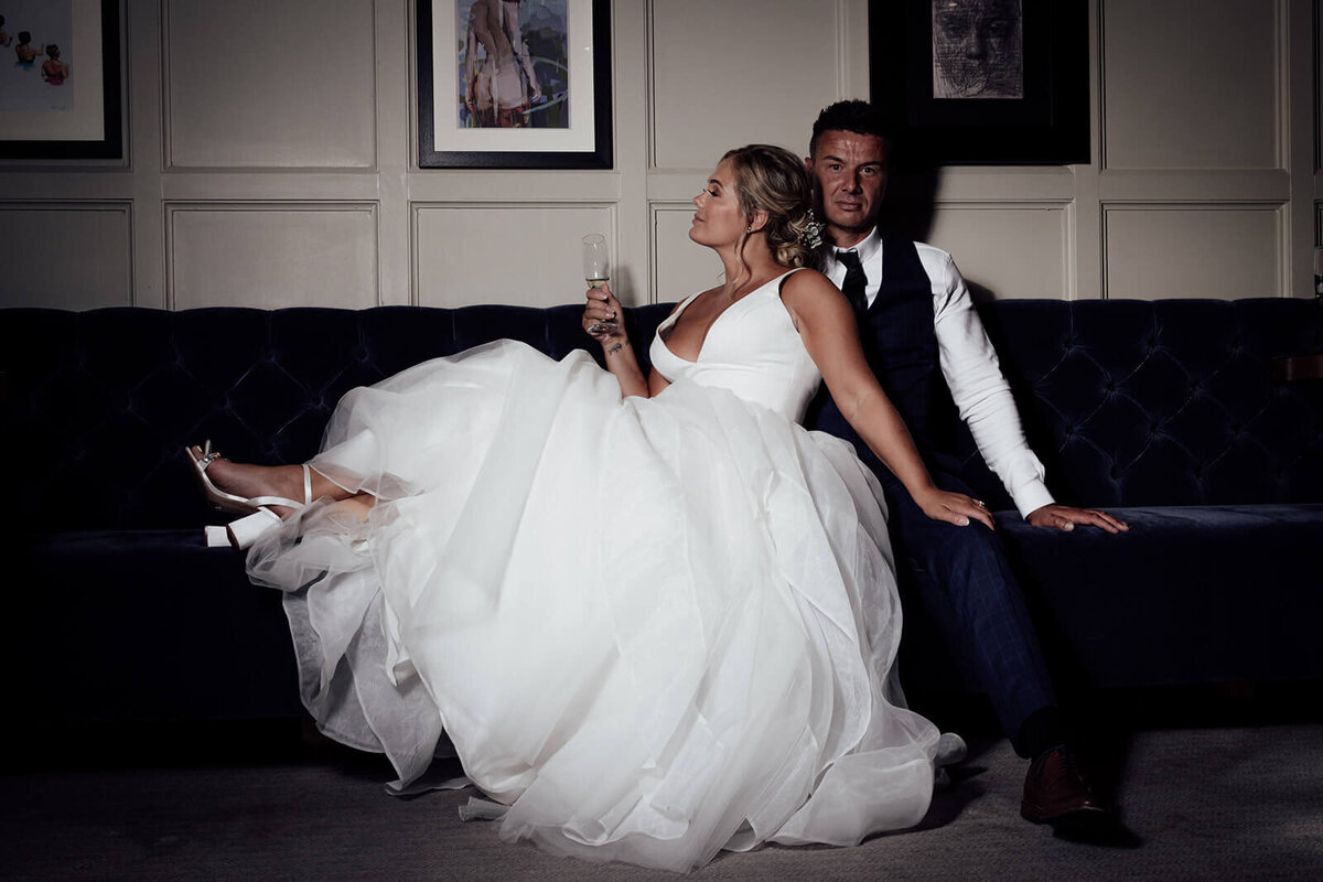 A wedding portrait of a couple sat in the Scotsman Edinburgh. The bride lays on her groom holding a glass of champagne