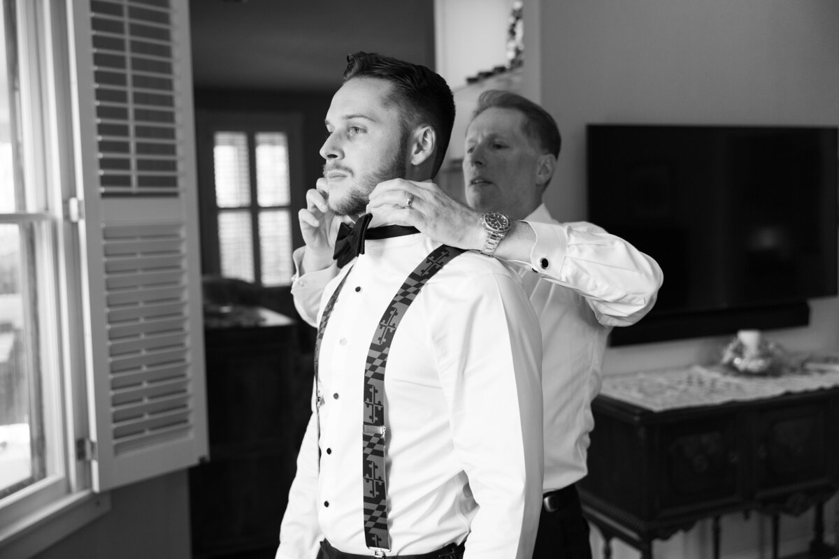 A person helping a groom put on a bow tie