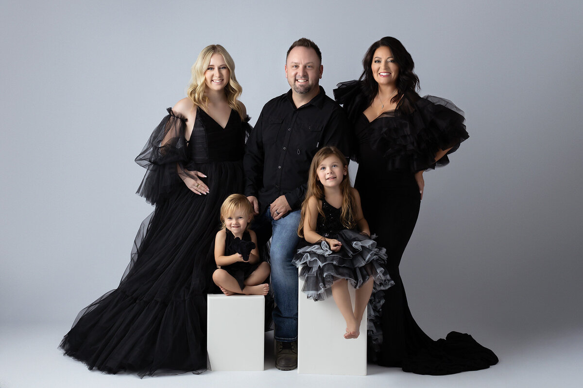 A beautiful family portrait captured in a sleek studio setting, styled in black gowns and a black shirt, by a Dallas family photographer.
