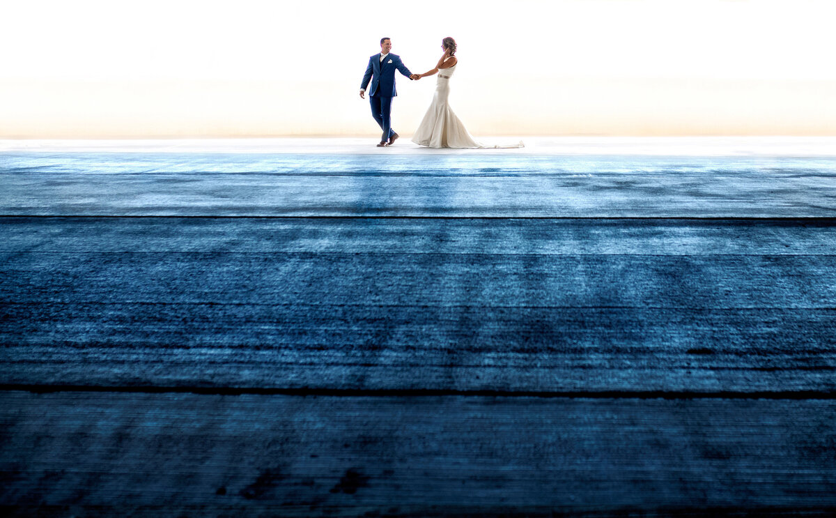 A couple in a parking garage walks across the blue tinted concrete.