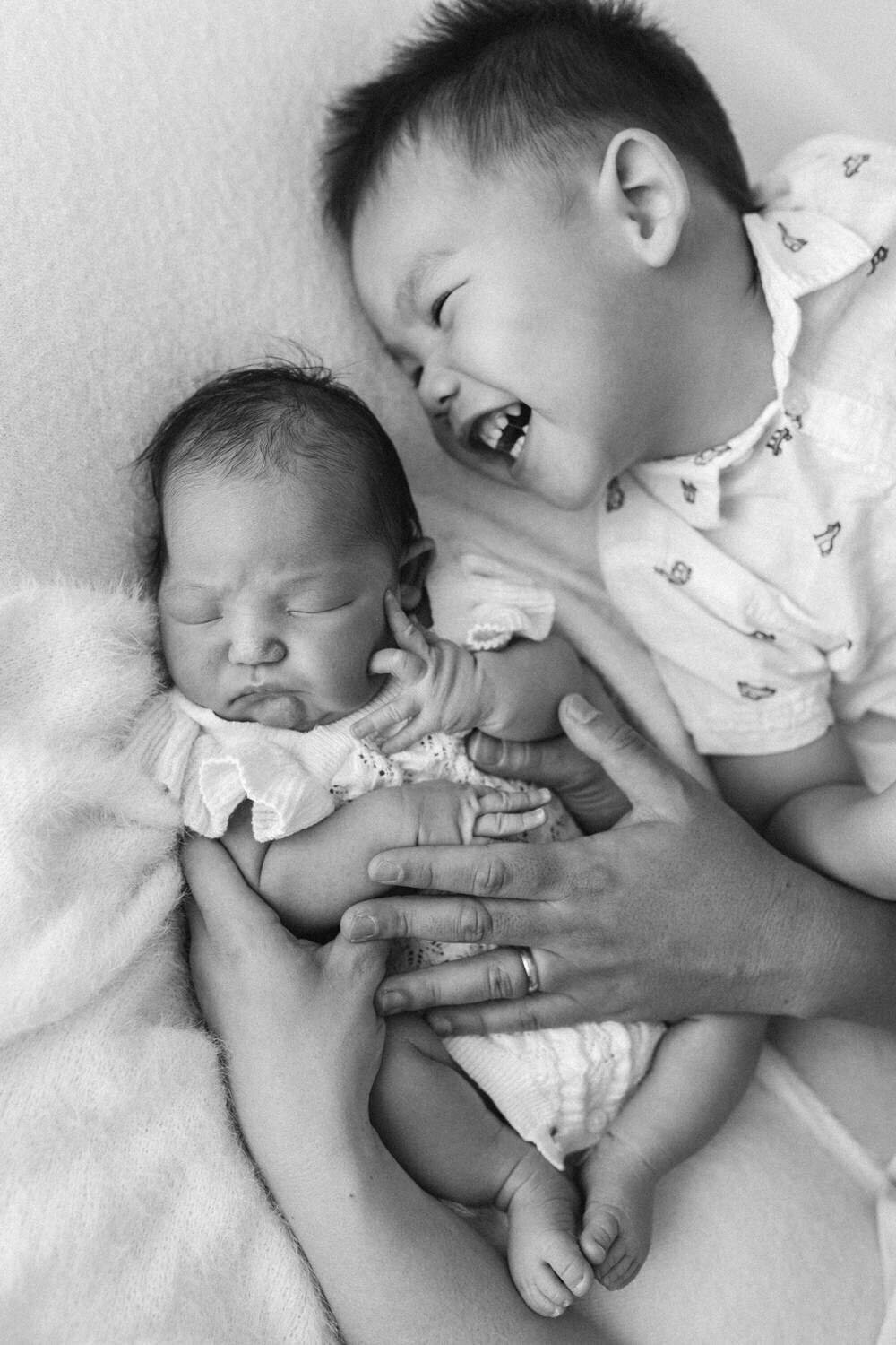 Big brother lies next to his little baby sister and laughs