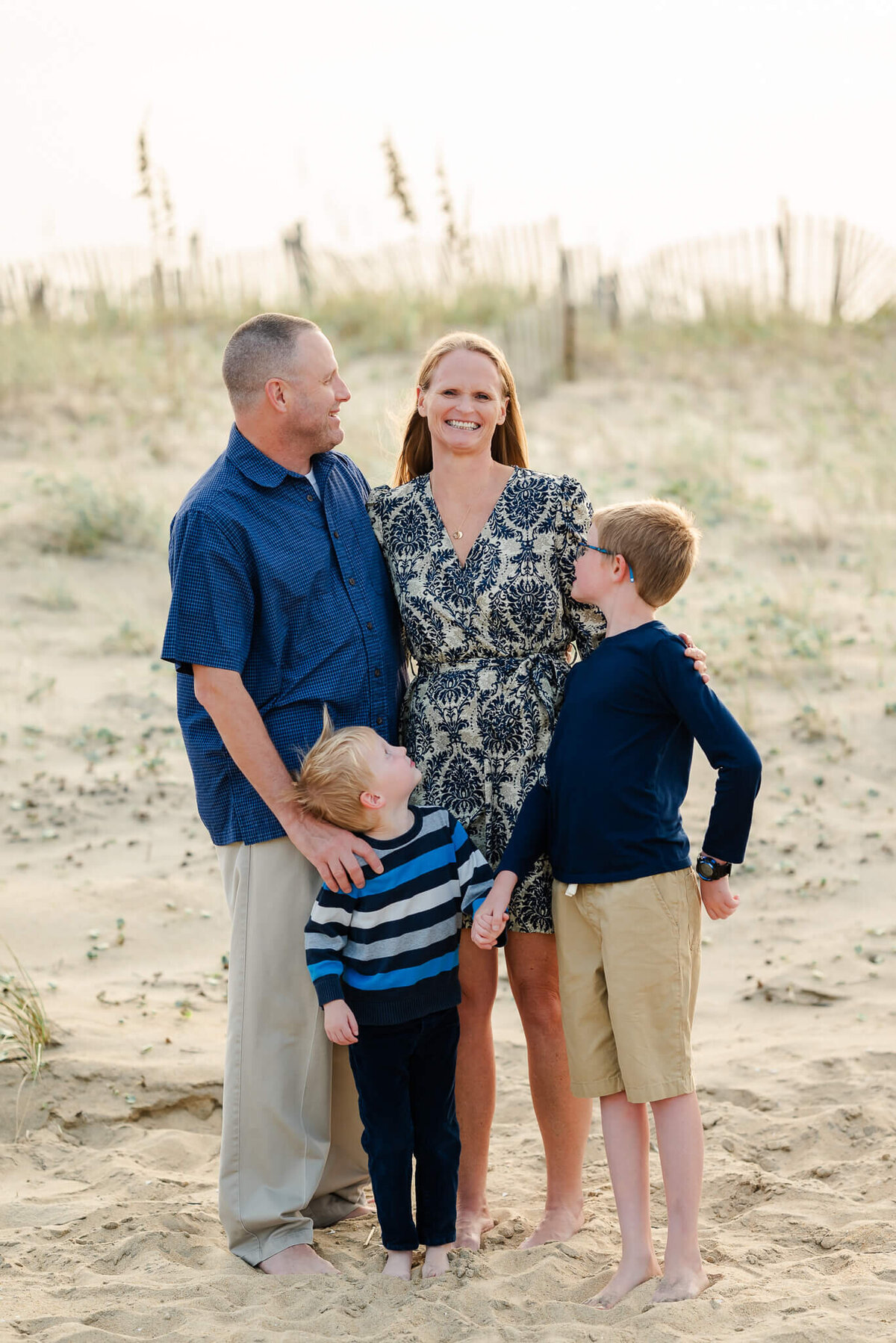 A dad and his two sons look lovingly at  the mom during a family photoshoot on the beach at the Outer Banks.