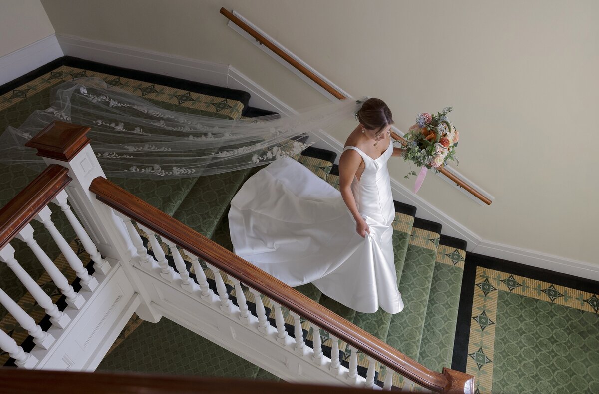 Bride walks down staircase at the Omni Mount Washington Hotel