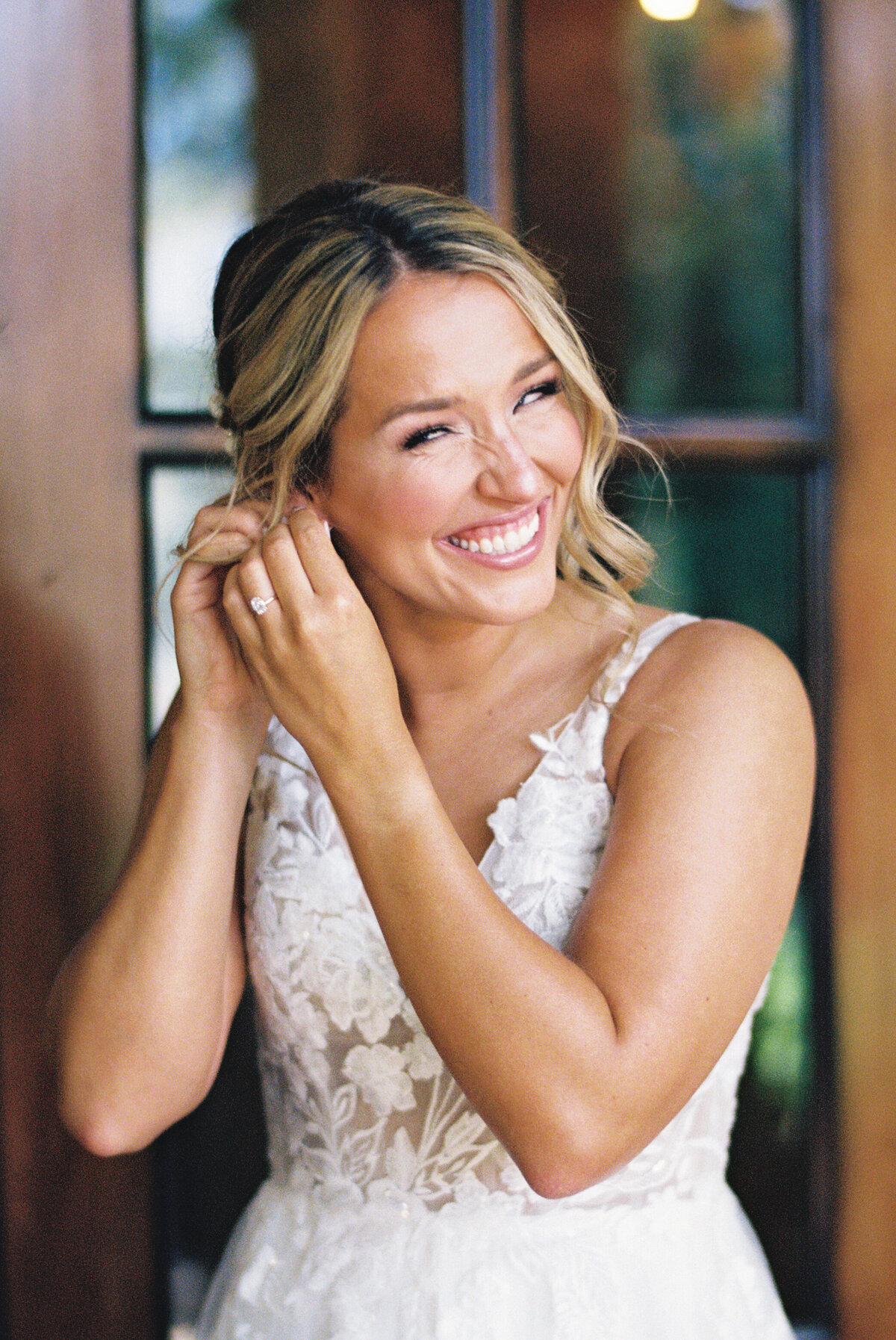 Bride smiling as she puts on pearl earrings, garden party wedding at Gervasi Vineyard