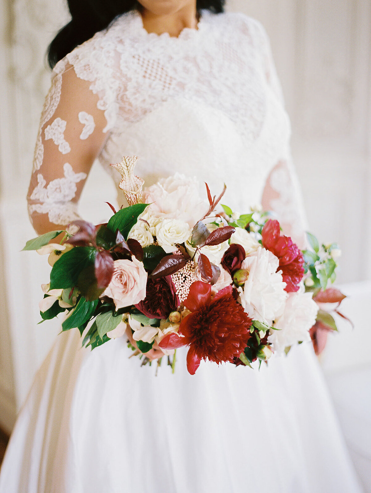 red peony bouquet with long sleeved lace wedding dress