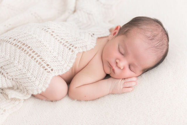 Baby sleeping peacefully on cozy tan blanket with a knit blanket covering up his back while he lays on tummy with face pointing towards the camera.