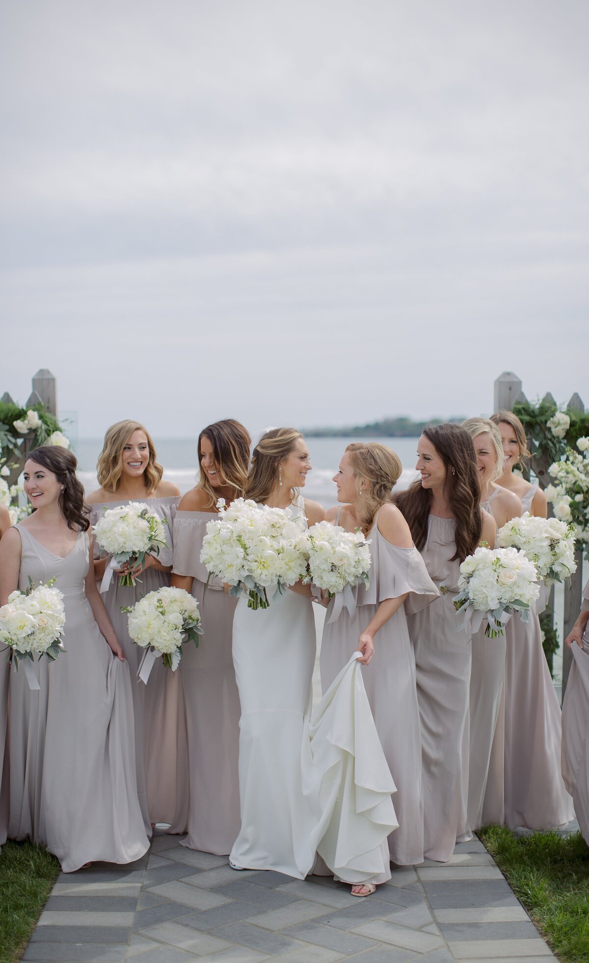 Bride walks with Bridesmaids in mauve dresses with ocean behind them during Newport wedding reception.