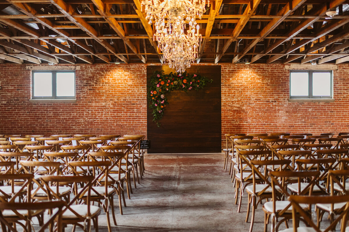 Wedding ceremony set up with chandeliers and walnut ceremony backdrop  with bright florals at the St Vrain