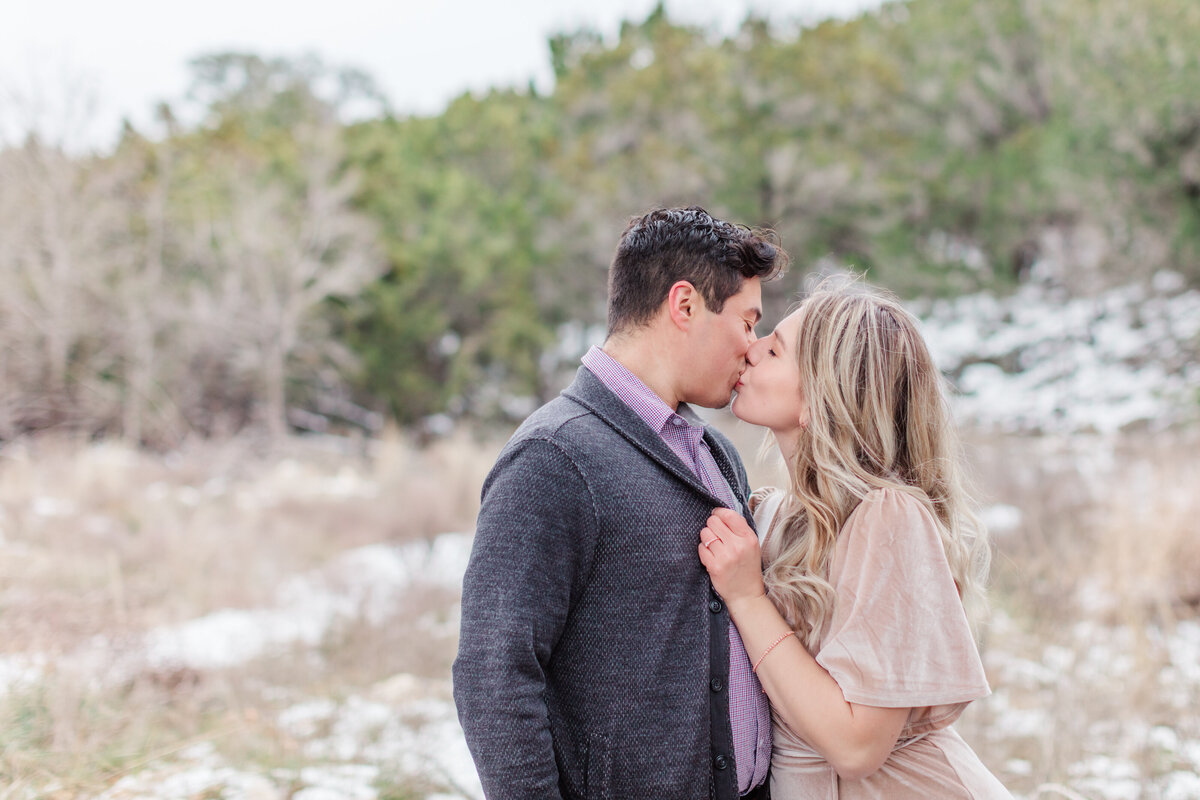 kissing in the woods with snow during engagement session by New Braunfels wedding photographer Firefly Photography
