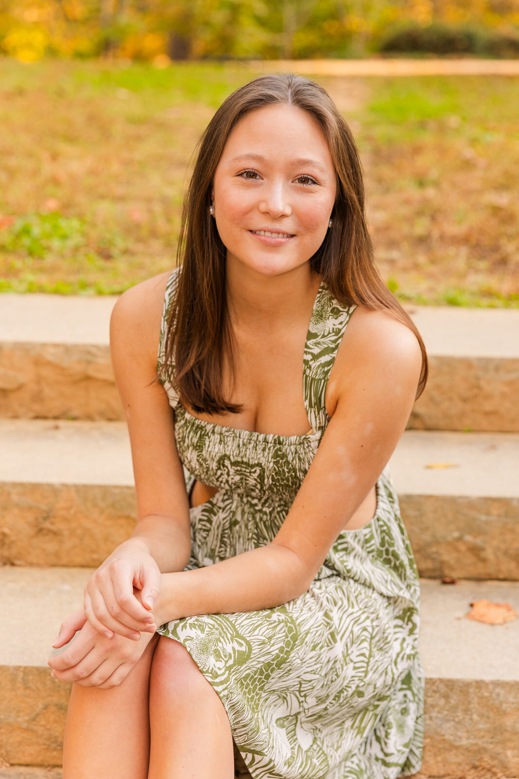 high school senior girl in a white and green dress sitting on stairs in a  park by Laure photography Atlanta