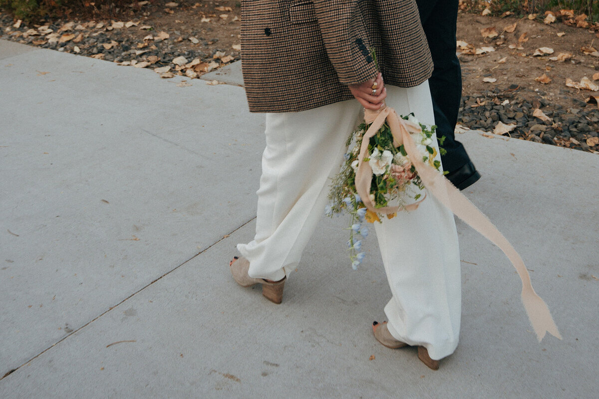 A faceless couple walking on a sidewalk and the woman is holding a bouquet of flowers down at her side.