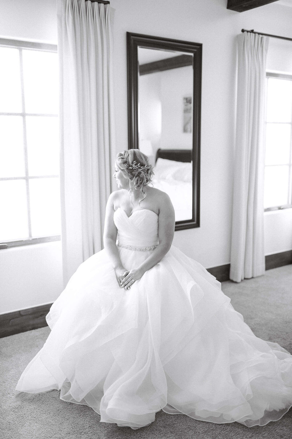 Elegant bride in fluffy wedding dress looks out window before ceremony