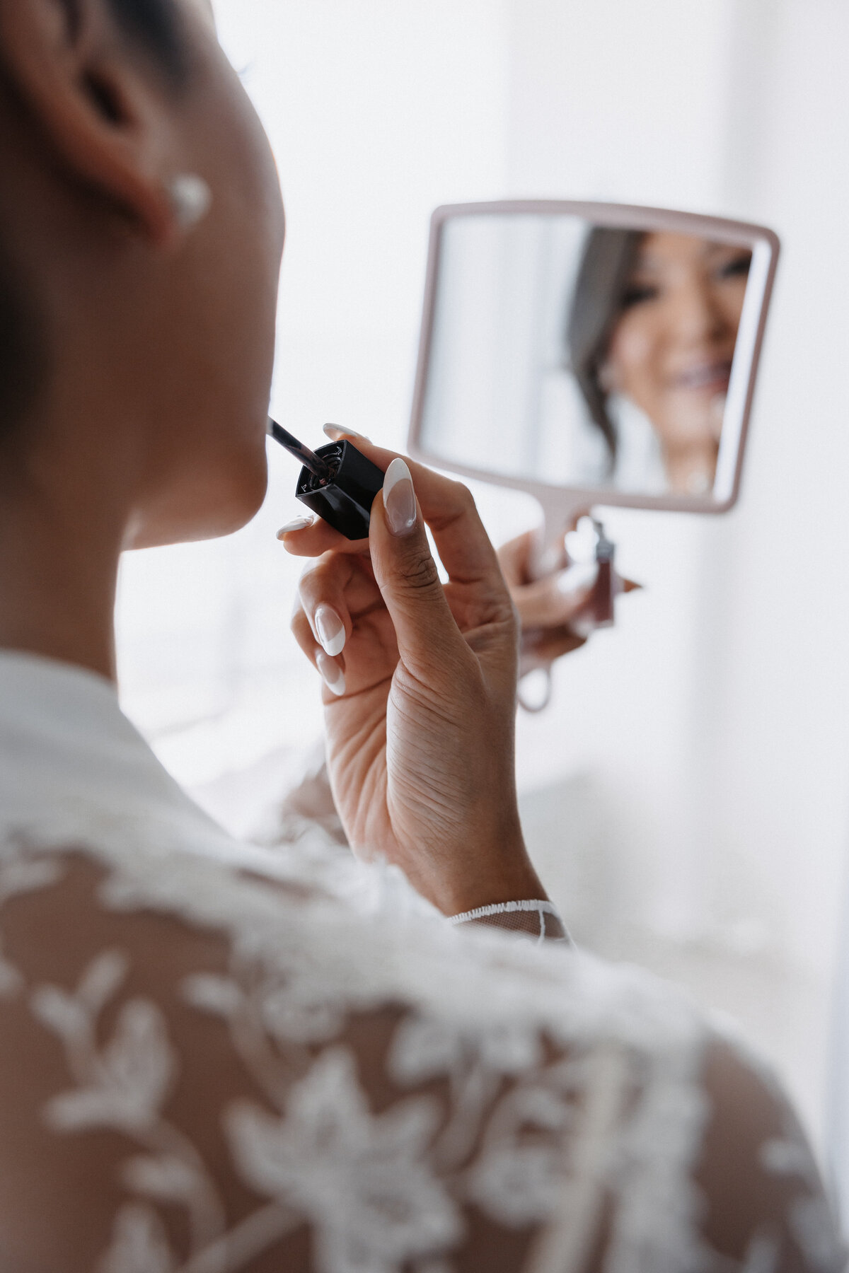 Bride in lace robe applying lipgloss in a mirror