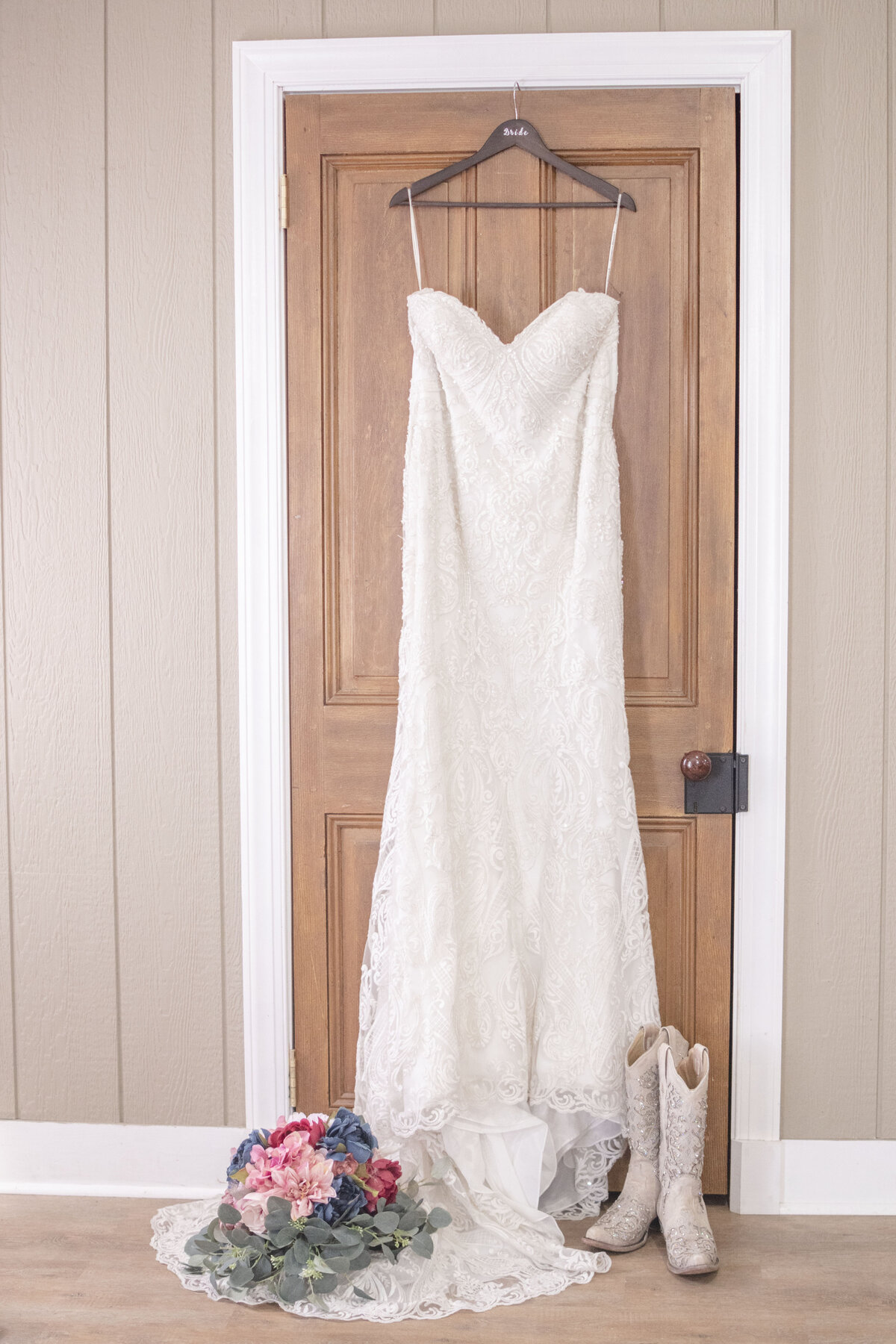 Wedding dress hanging with bouquet and boots