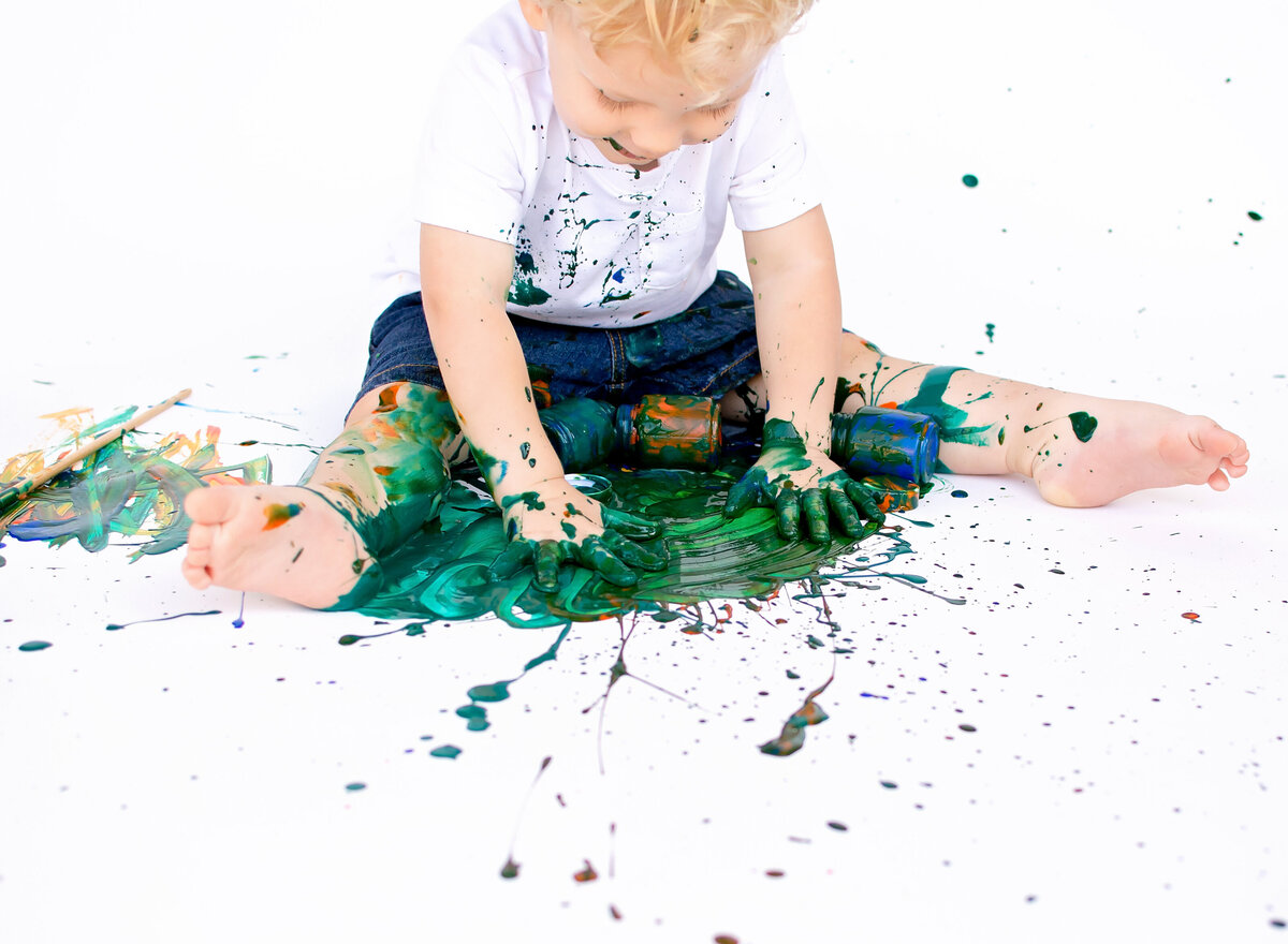 Painting photoshoot, little boy is playing in green paid wearing a white shirt and blue shorts