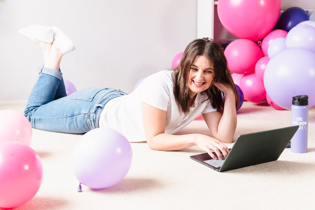brand photo of woman  lying with her laptop among balloons