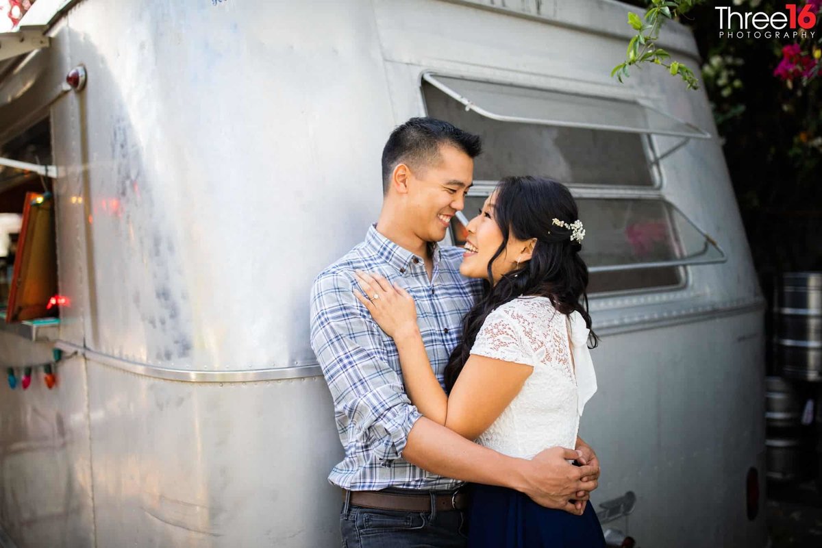 Engaged couple embrace as they lean up against an old camper trailer in the LA Art District