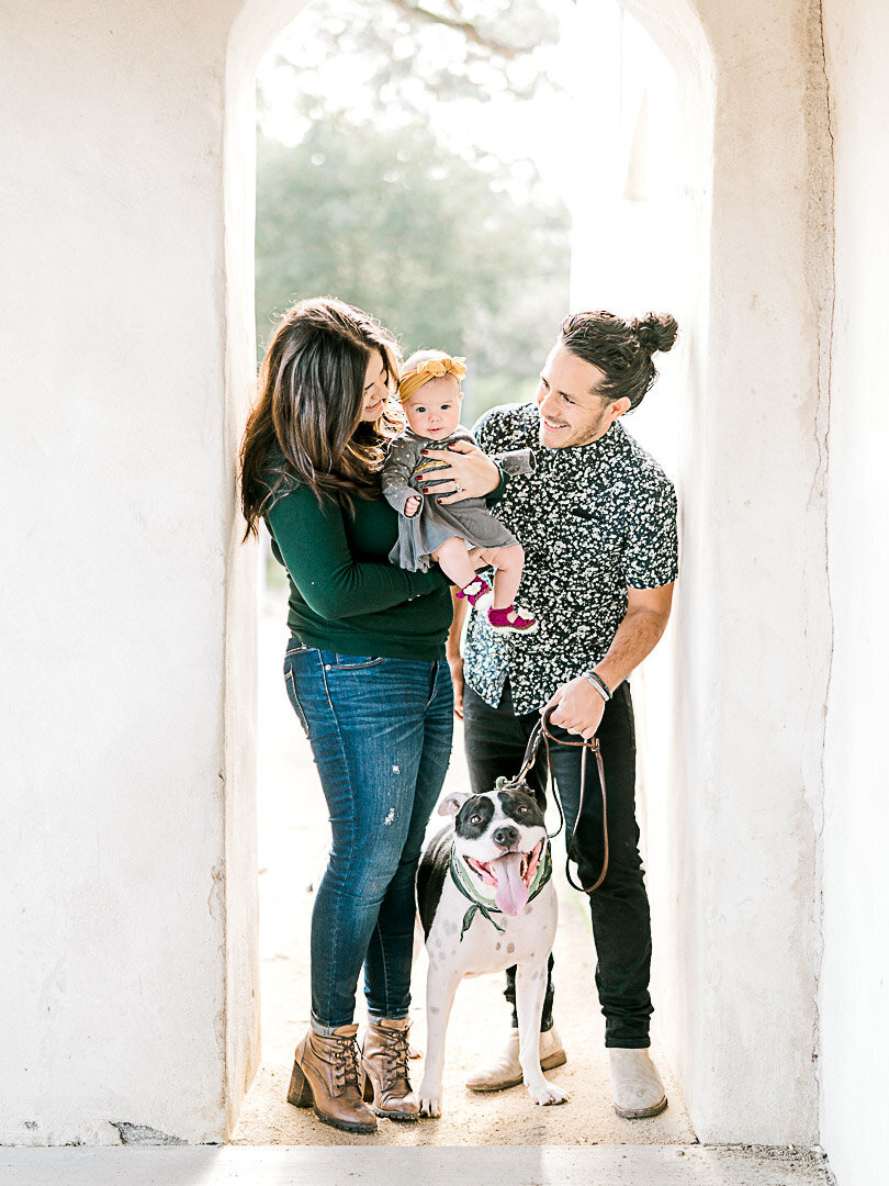 Family with their newborn and dog smiling at daughter and being photographed by Vanessa Montano