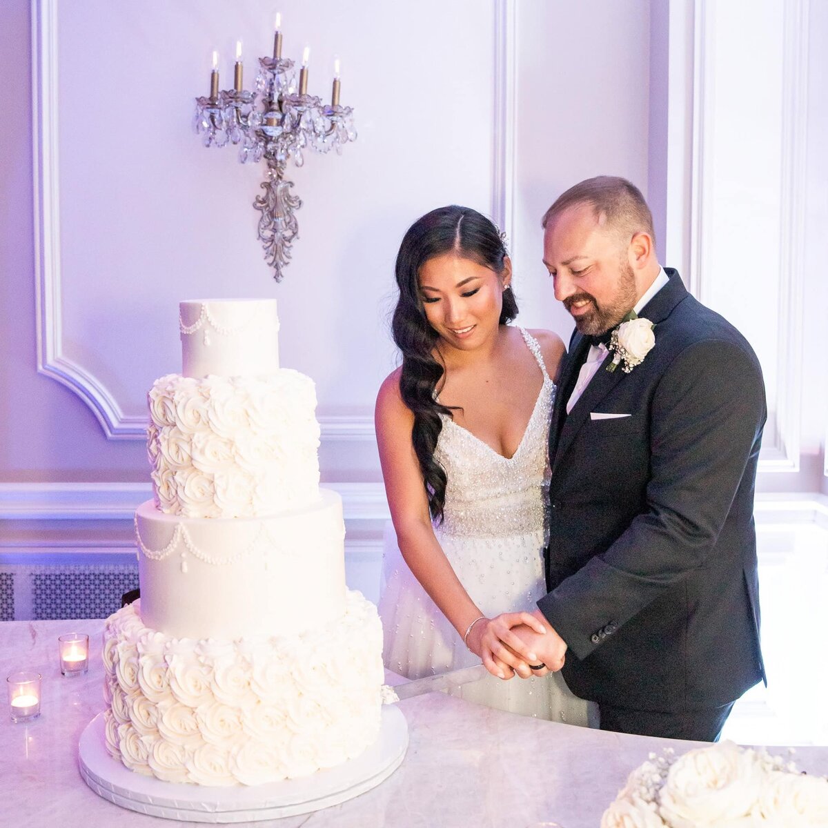 Bride and Groom cut elegant four layer wedding cake with piped roses in a purple lit room at the Mansion on Main in New Jersey.