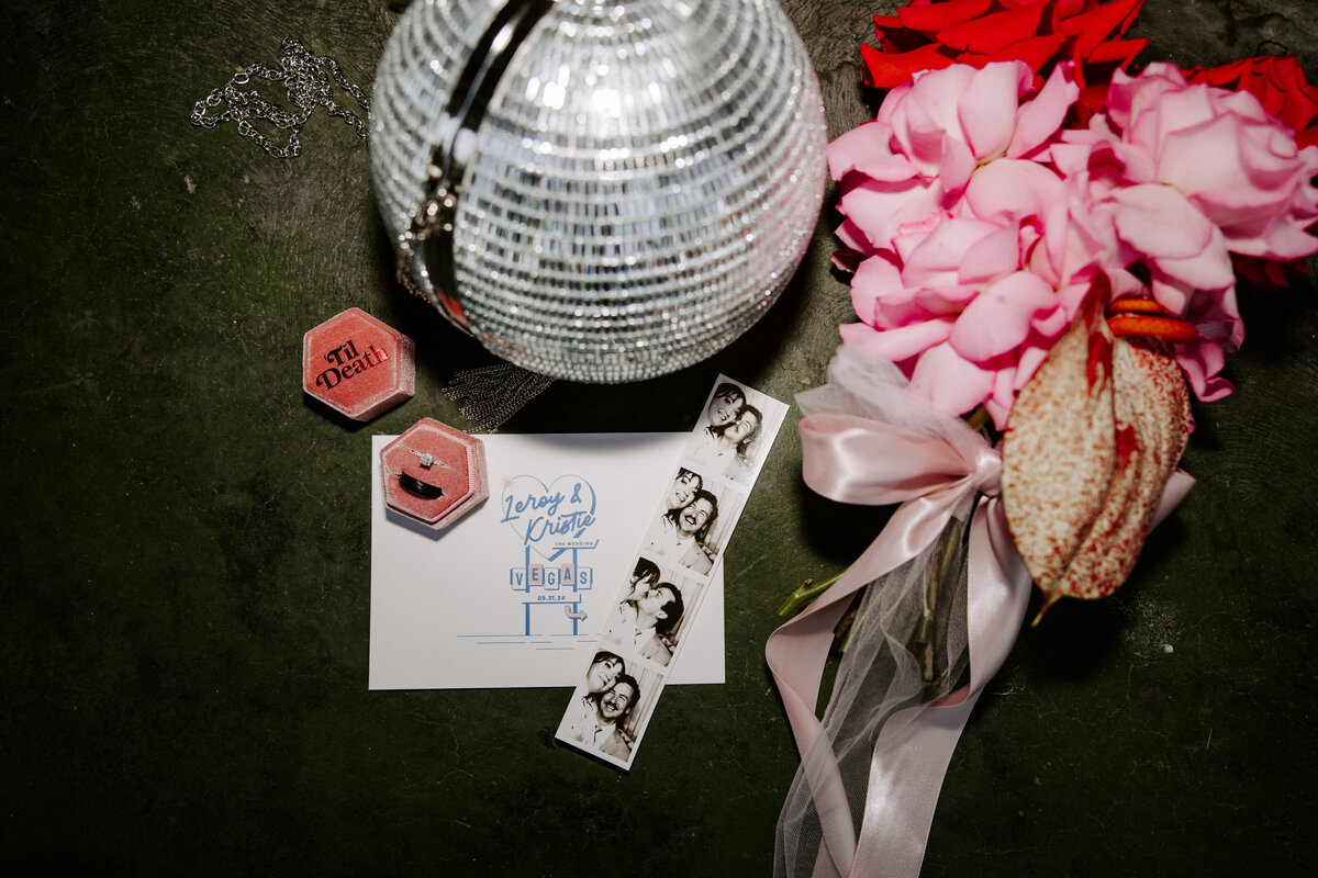 A flat lay of elopement details including a disco ball bag, flowers, and invitation.