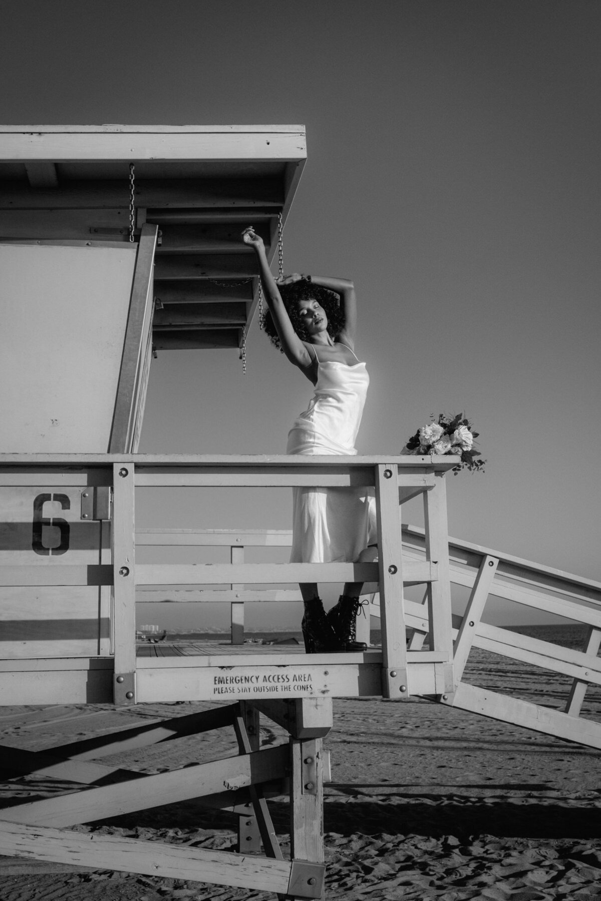 Auf einem Rettungsschwimmer-Haus stehend posiert die Braut mit hoch gestreckten Armen.