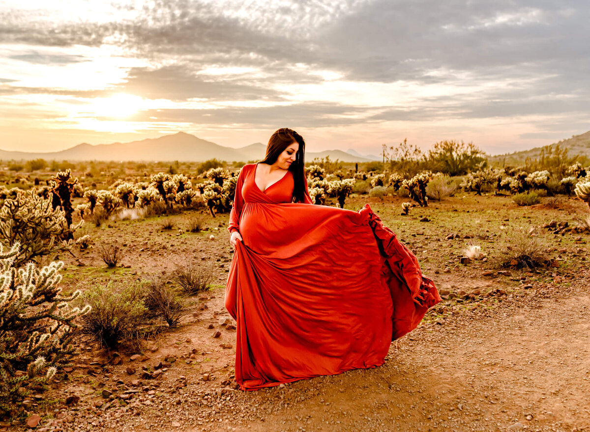 mom playing with flowy, rust maternity dress for photographer in Arizona