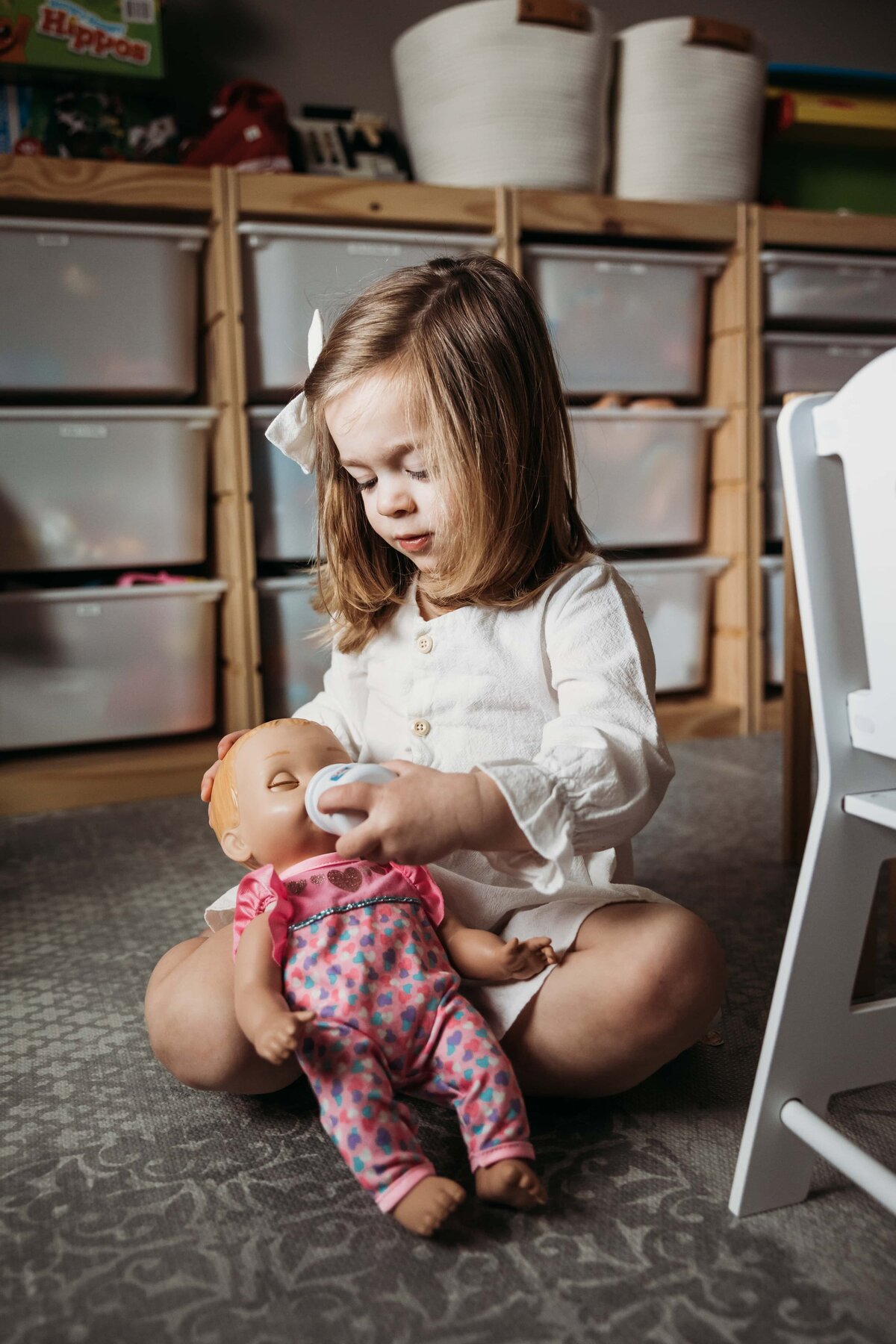 A young child captures a diy family photo moment by feeding a doll with a toy bottle in a playroom.