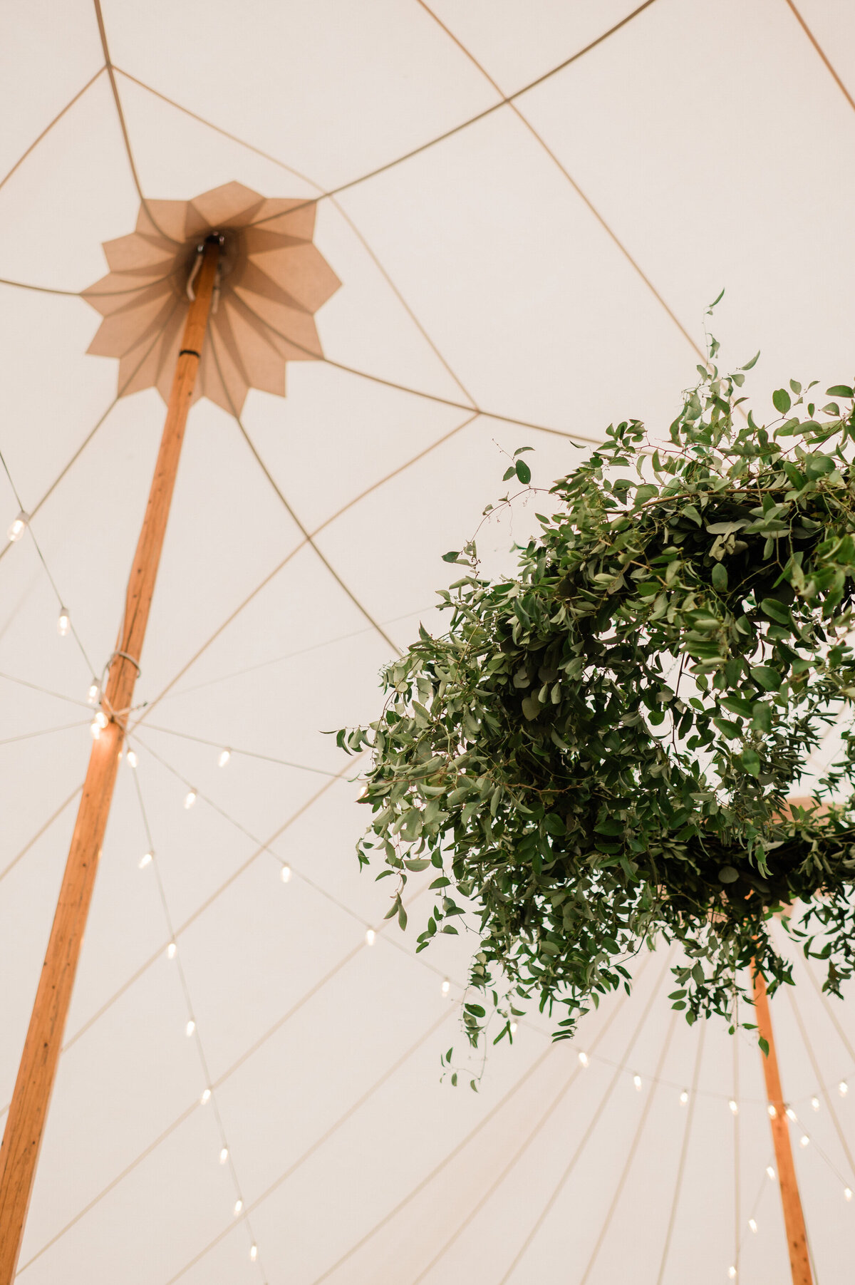 A wreath hangs from the ceiling of a tent, surrounded by string lights.