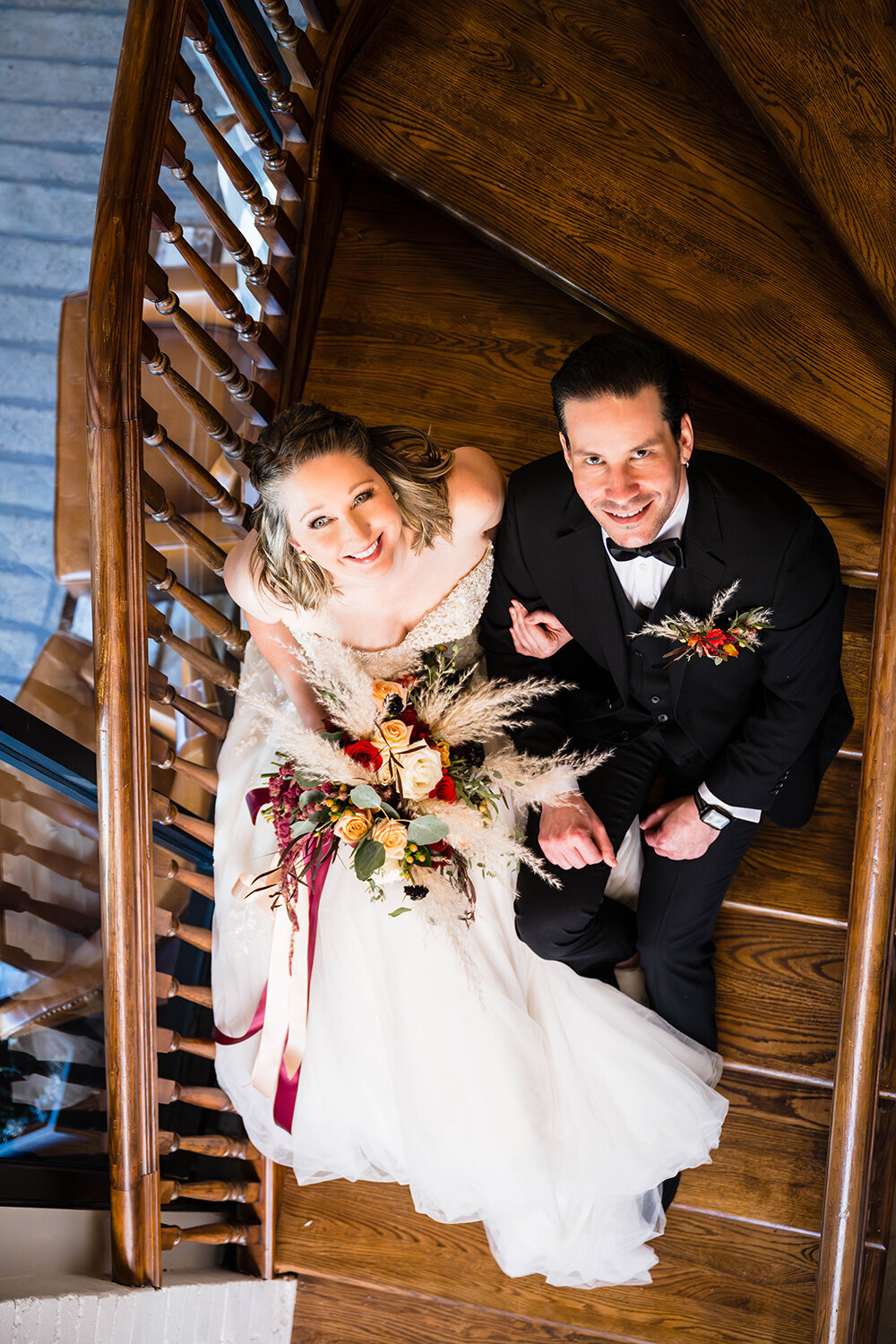 A couple on their elopement day sit side-by-side on a stairwell in the renovated Fire Station One hotel in Roanoke, Virginia and look up and smile to have their photo taken.