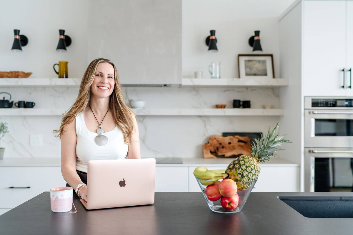 entrepreneur working on laptop in kitchen with bowl of fruit on the counter
