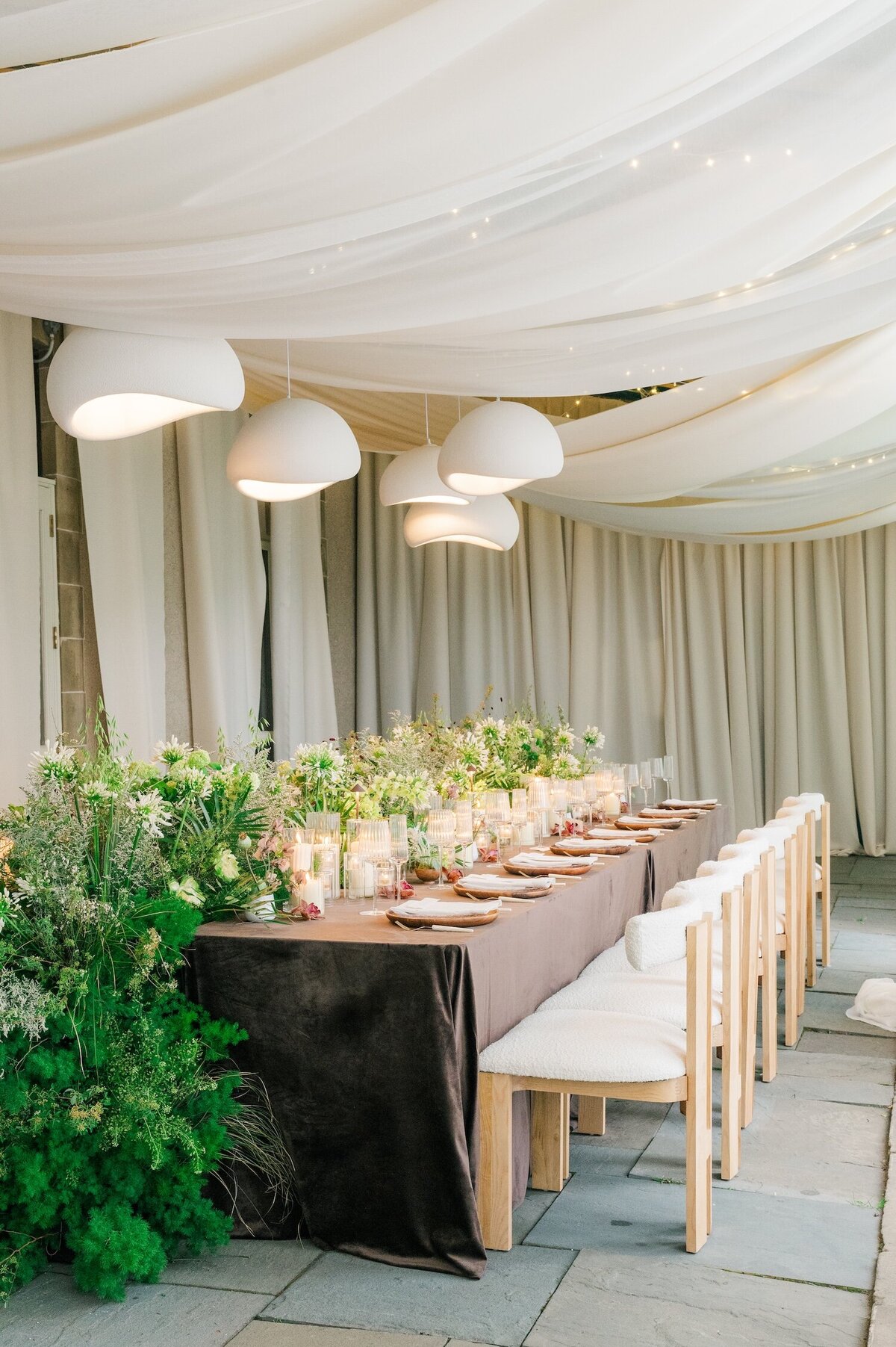 A table setting with a brown tablecloth, a cascading floral arrangement, and plates and candles on the outdoor terrace at Glen Manor House. 