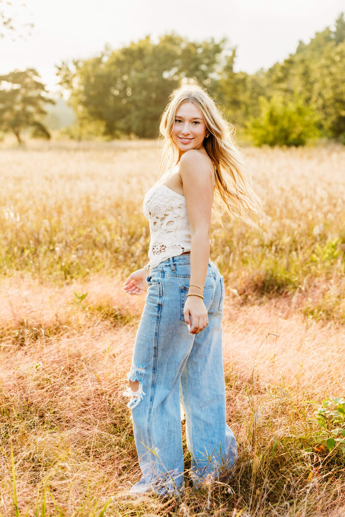 Green Bay high school senior in a lace top and jeans, spinning in a field  and looking back captured by Ashley Kalbus Photography