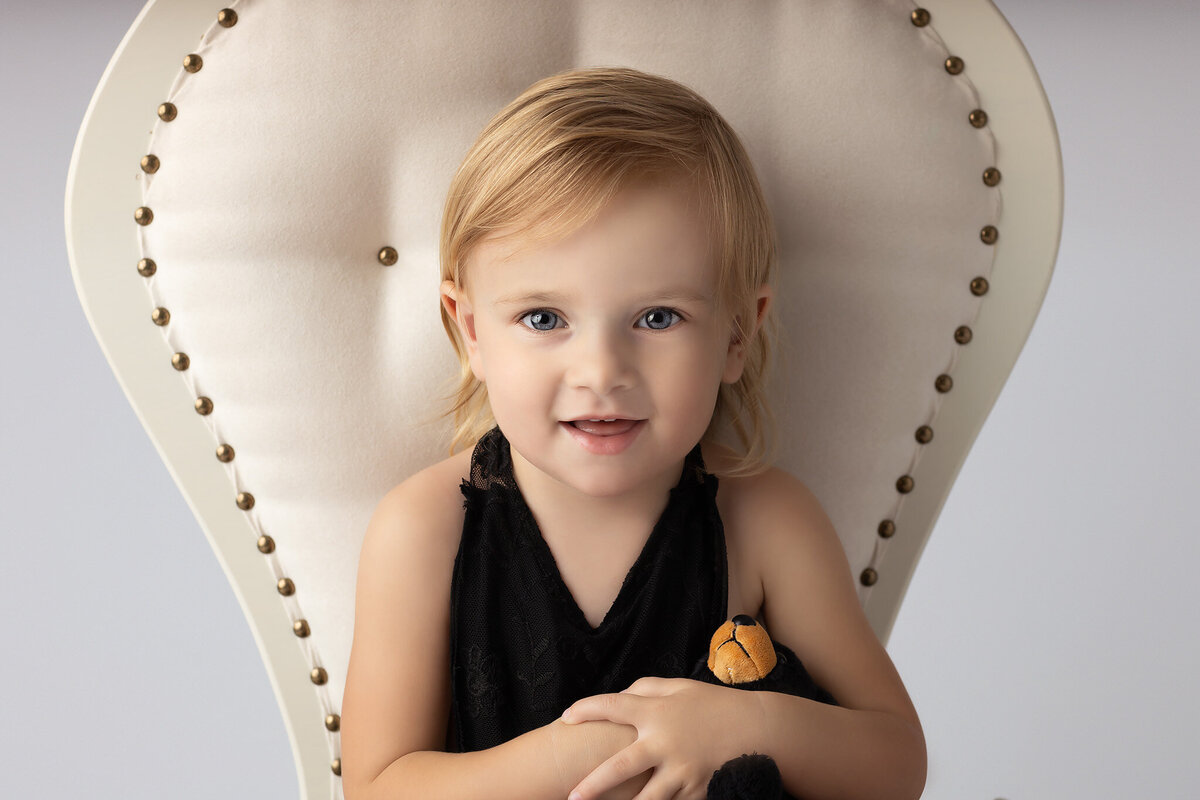 Close-up of a toddler smiling while holding a stuffed bear, photographed by a Dallas family photographer.