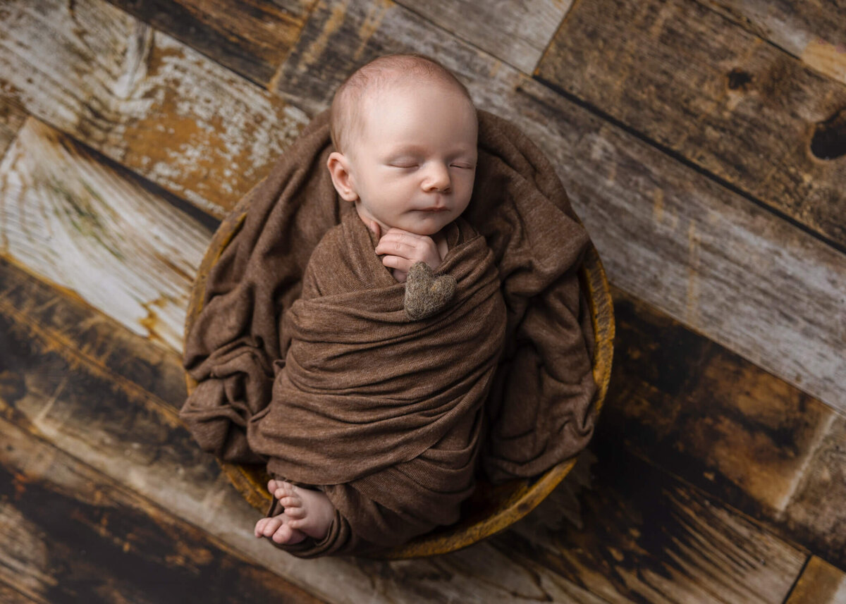 newborn baby sleeping in a wooden bowl wrapped in a brown fabric