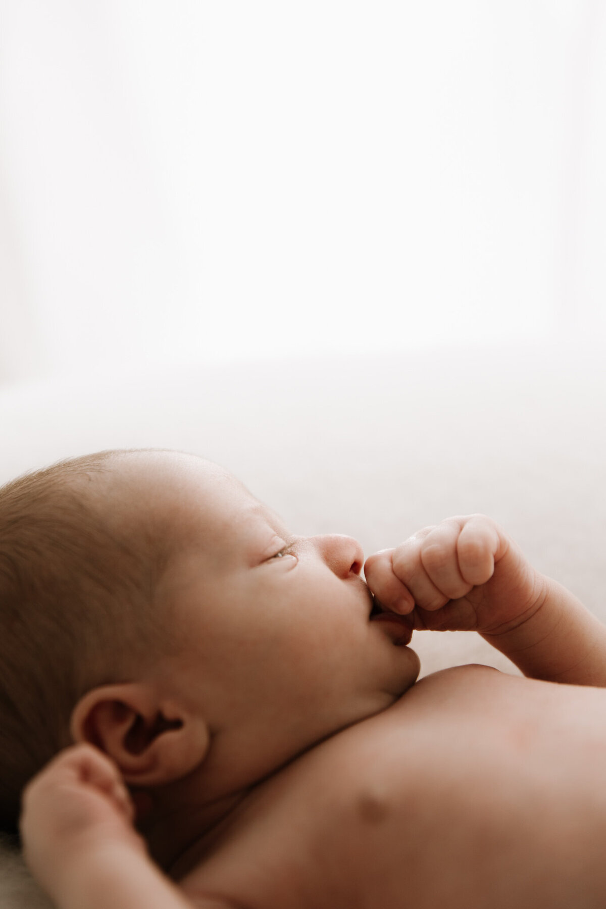 Newborn baby peacefully sucking thumb while lying on a soft surface, captured in gentle natural-style lighting by a Sydney newborn photographer.