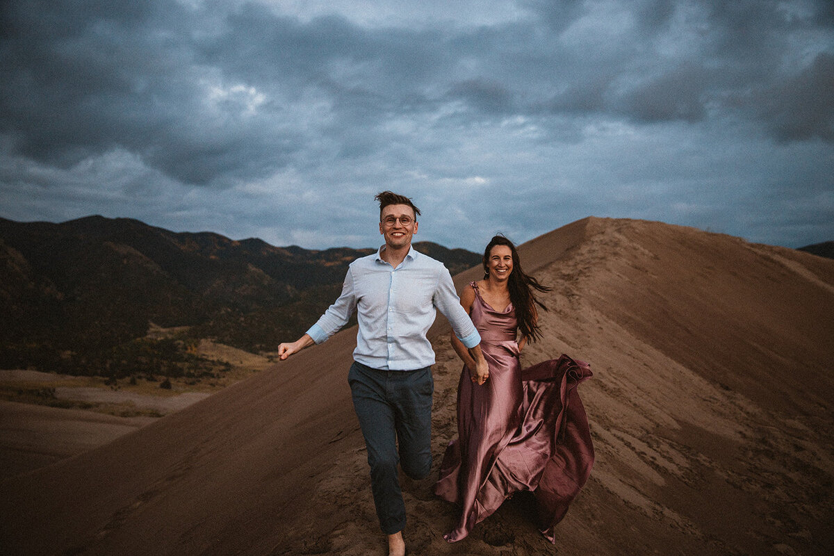 man and woman wearing pink dress runs down great sand dunes national park