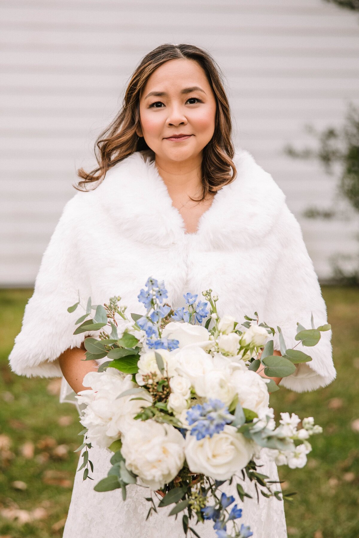 A bride wearing a white fur jacket holds a bouquet