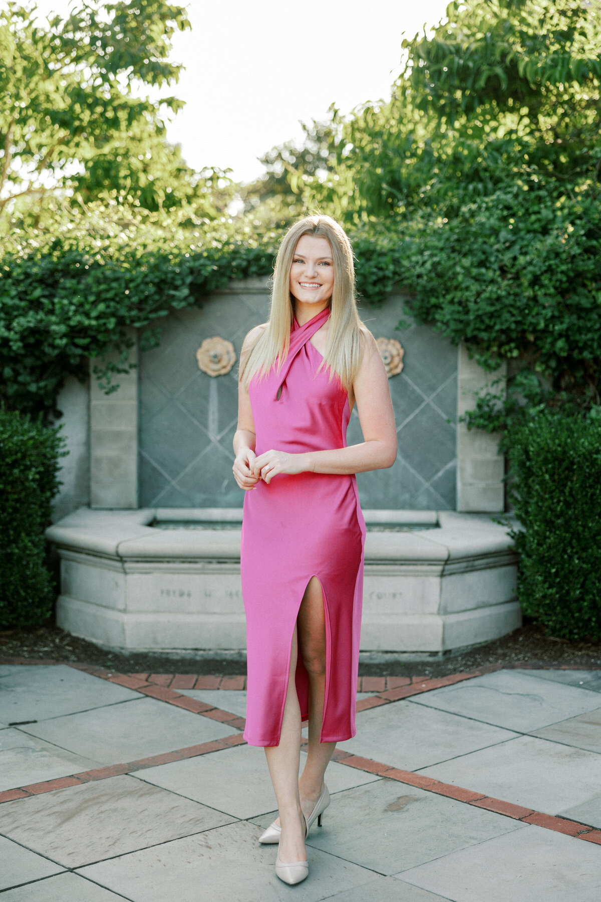 Woman in pink dress poses in front of stone fountain in Columbus park.