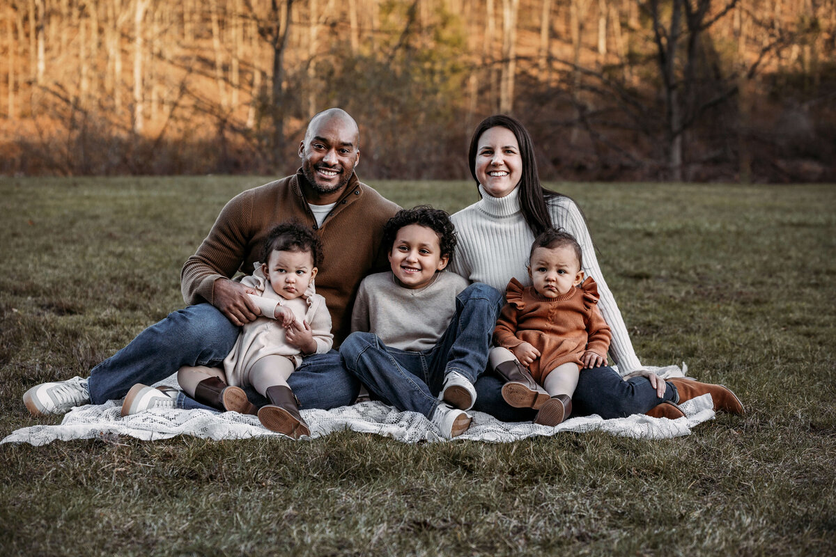 family of 5 with 2 toddlers and a young boy wearing fall colors and jeans sittting on a blanket during a fall sunset family session