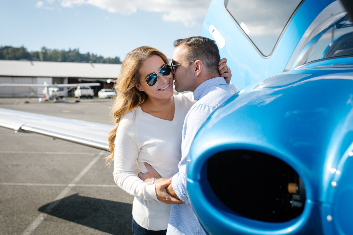 An engaged couple flirting next to a small airplane.