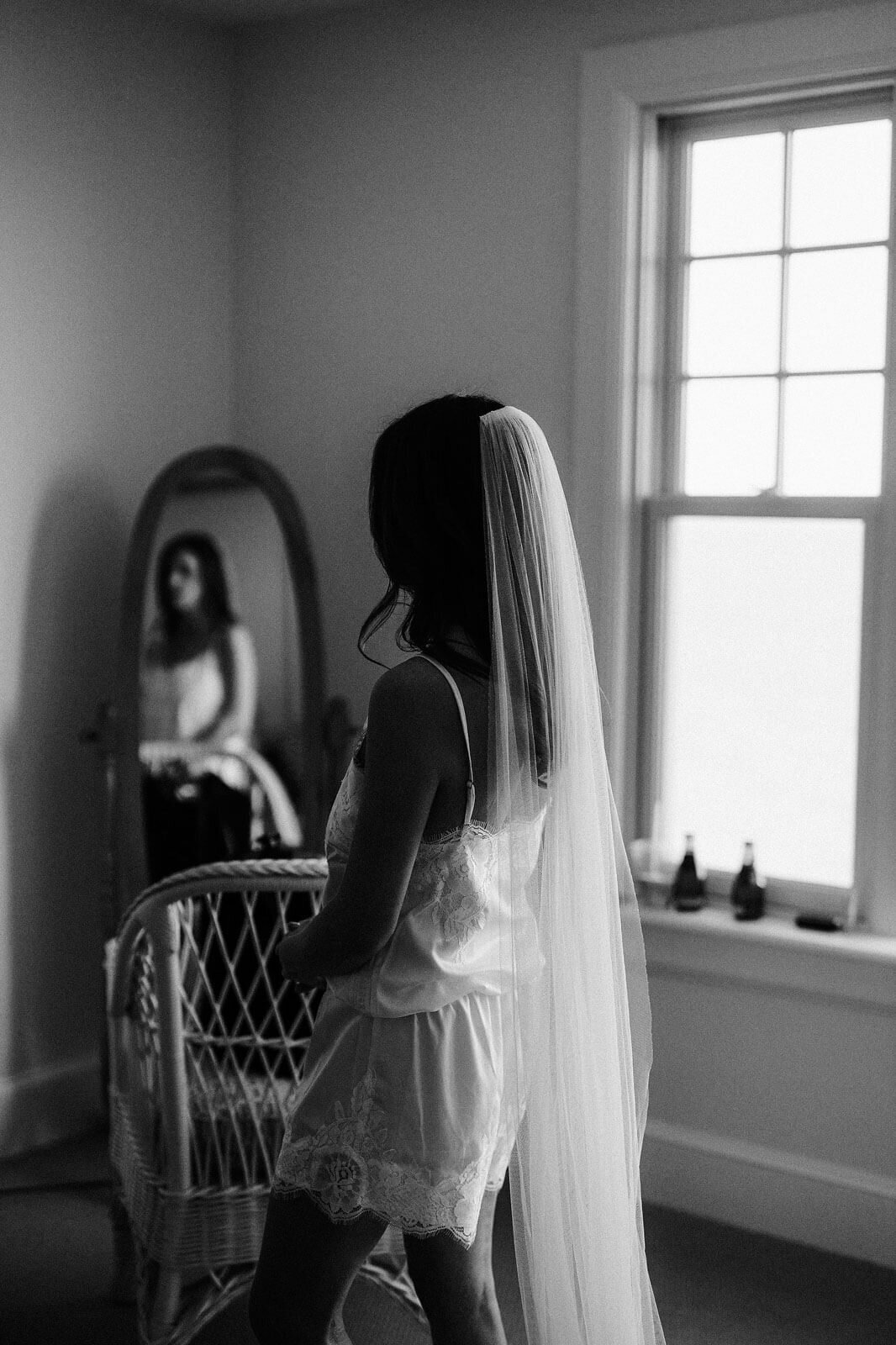 The bride is standing in a room, her reflection is shown in the mirror, at Wianno Club, Cape Cod, MA.