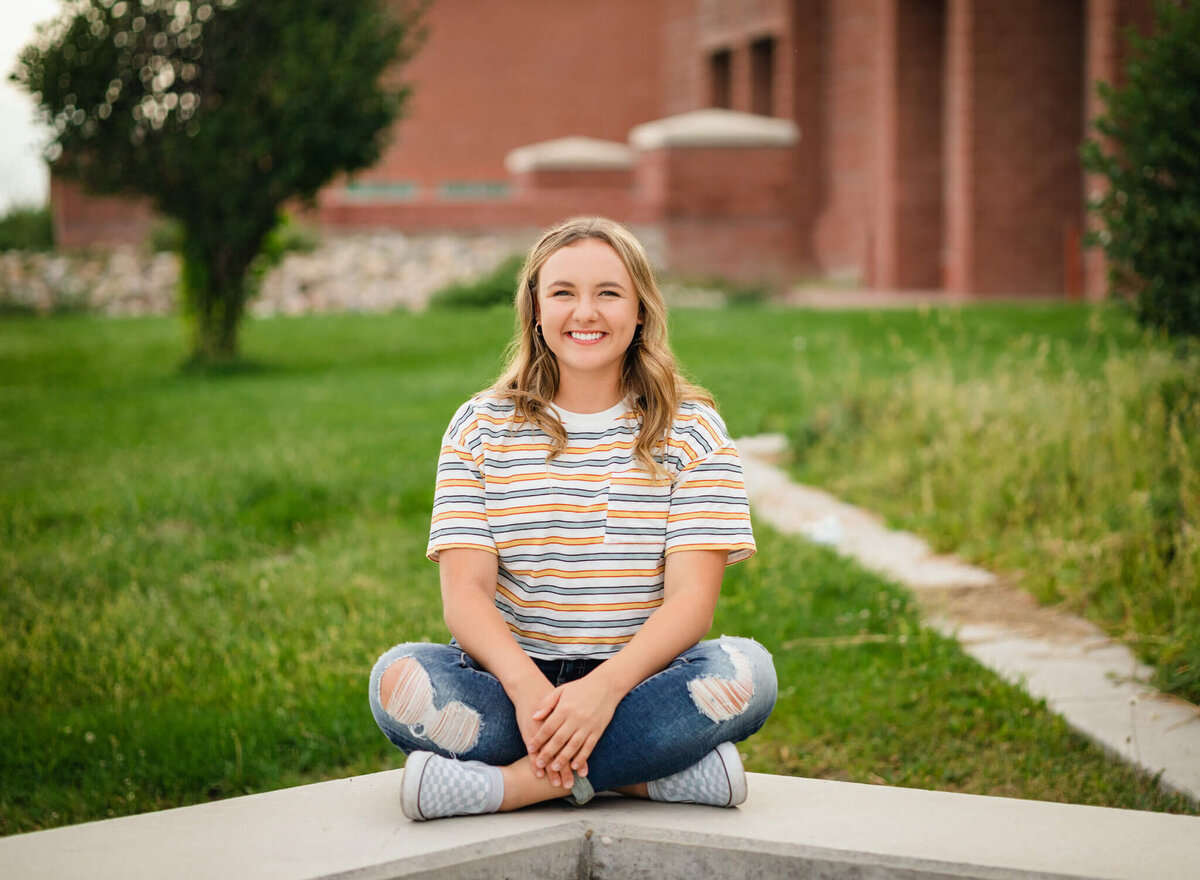 teenage girl sitting criss cross on a  cement bench in front of her high school