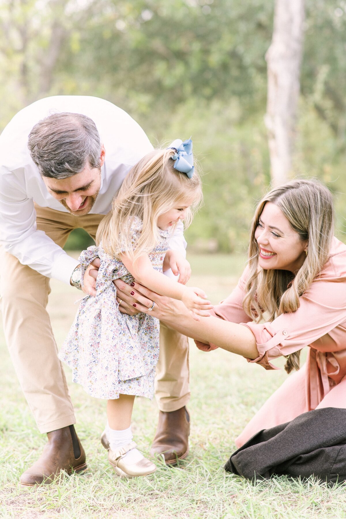 Best Houston family photographer captures joyful, candid moments of parents and kids playing in a sunlit park.