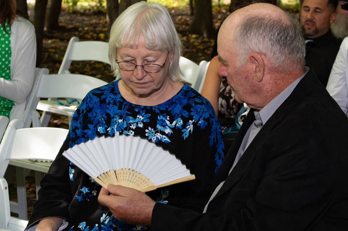elderly man fans wife with at hot outdoor ceremony