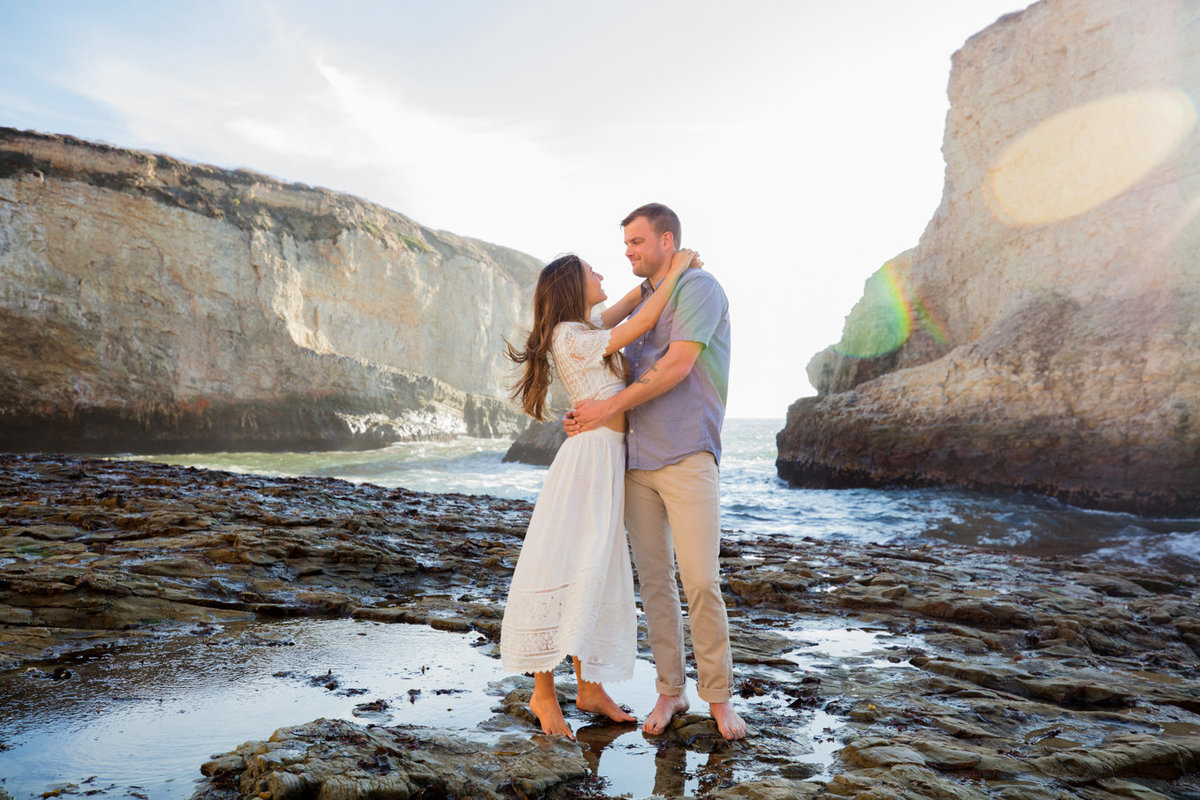Engagement session in davenport, california, couple hugging on beach with natural light and backlit